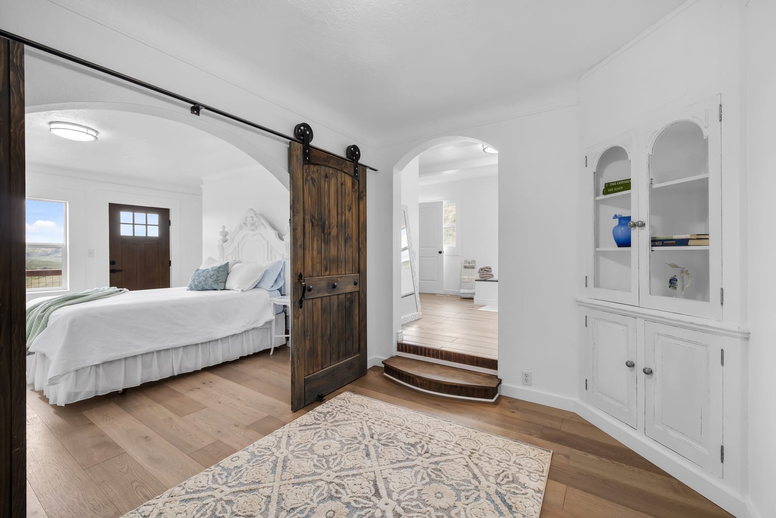 Residential bedroom with a made bed, a sliding barn door, and warm wood floors at the New Frontier Recovery Center property in Huntley, Montana
